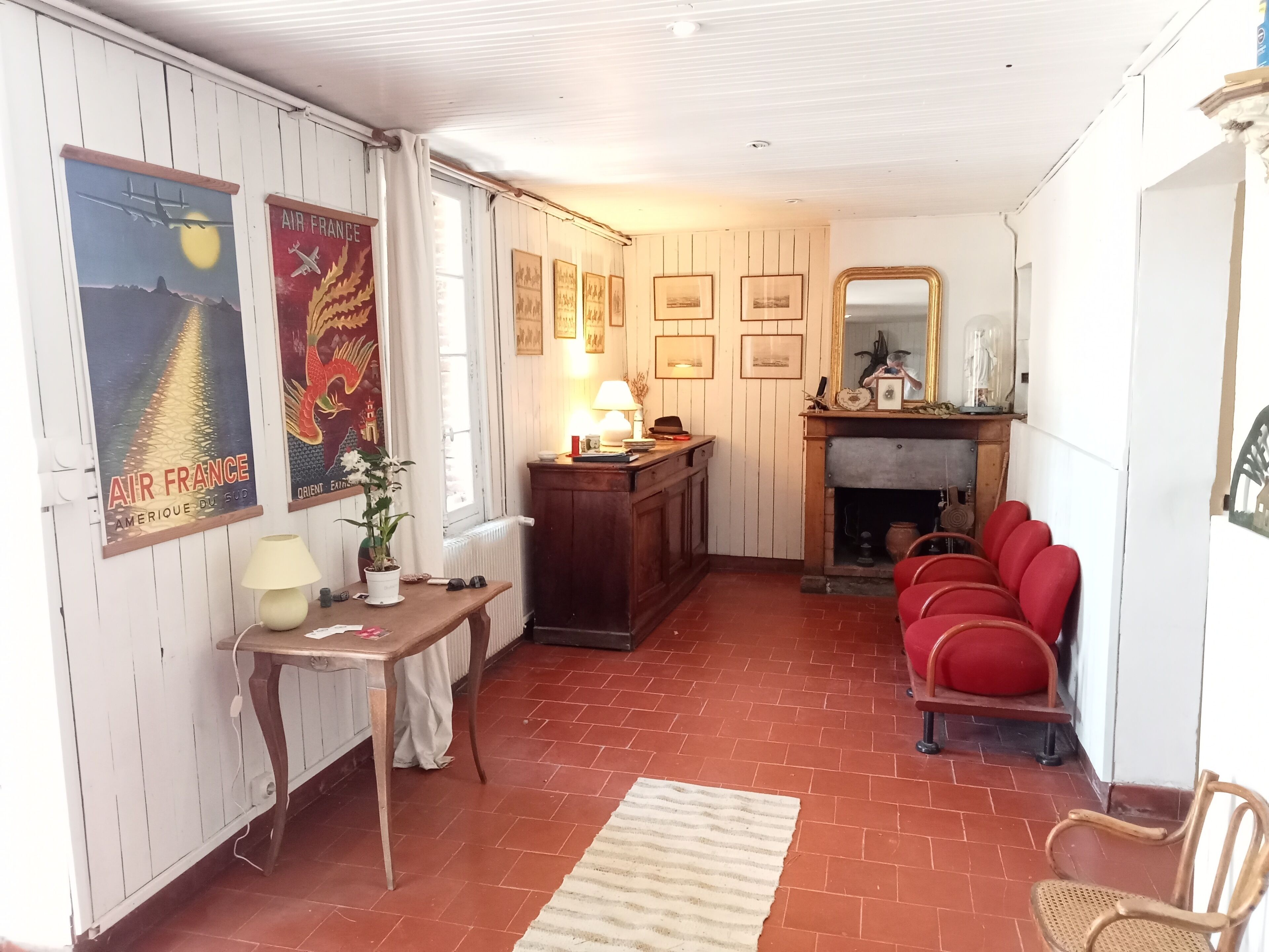 Une pièce chaleureuse avec une cheminée, une table en bois avec une lampe, des chaises rouges et un tapis.