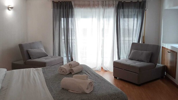 A modern hotel room with a large bed, two armchairs, a small sofa, and a wooden floor. - B & B 30 mt dal duomo (Benevento)