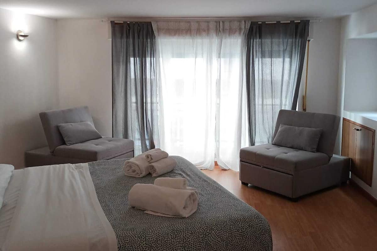 Una habitación de hotel moderna con una cama grande, dos sillones, un pequeño sofá y piso de madera.