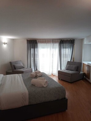 Una habitación de hotel moderna con una cama grande, dos sillones, un pequeño sofá y piso de madera.