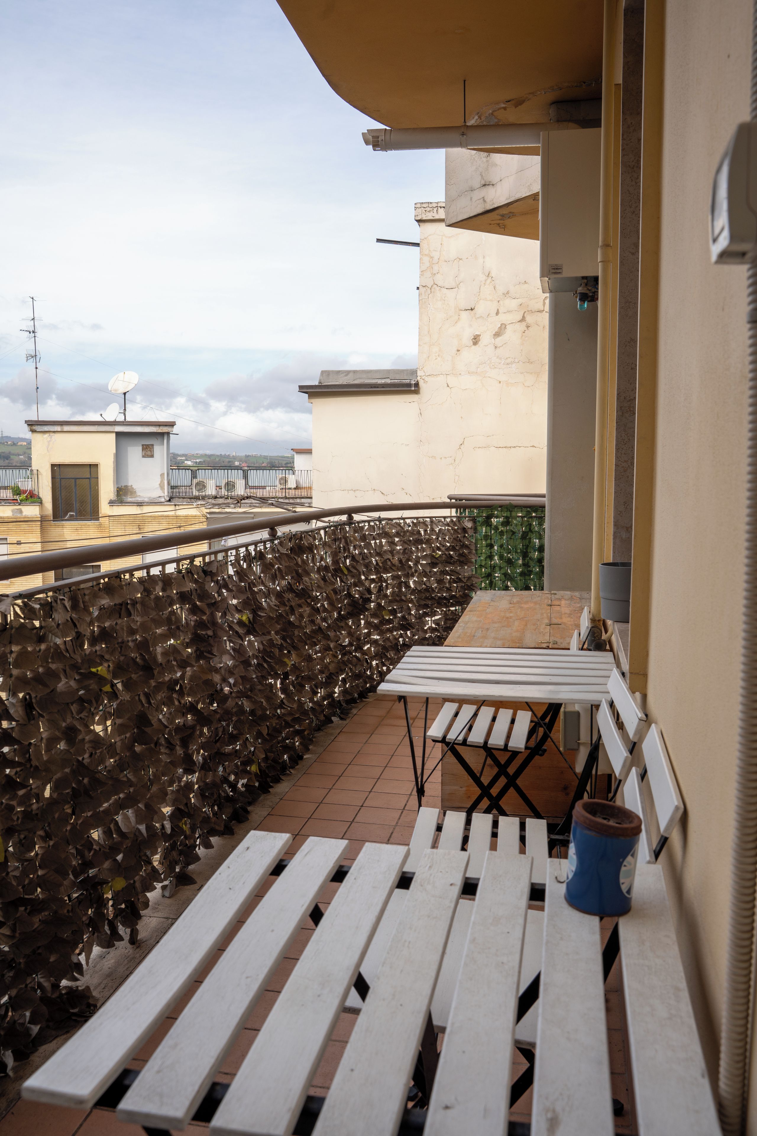 A rooftop terrace with a table and benches, a view of the cityscape, and a satellite dish.