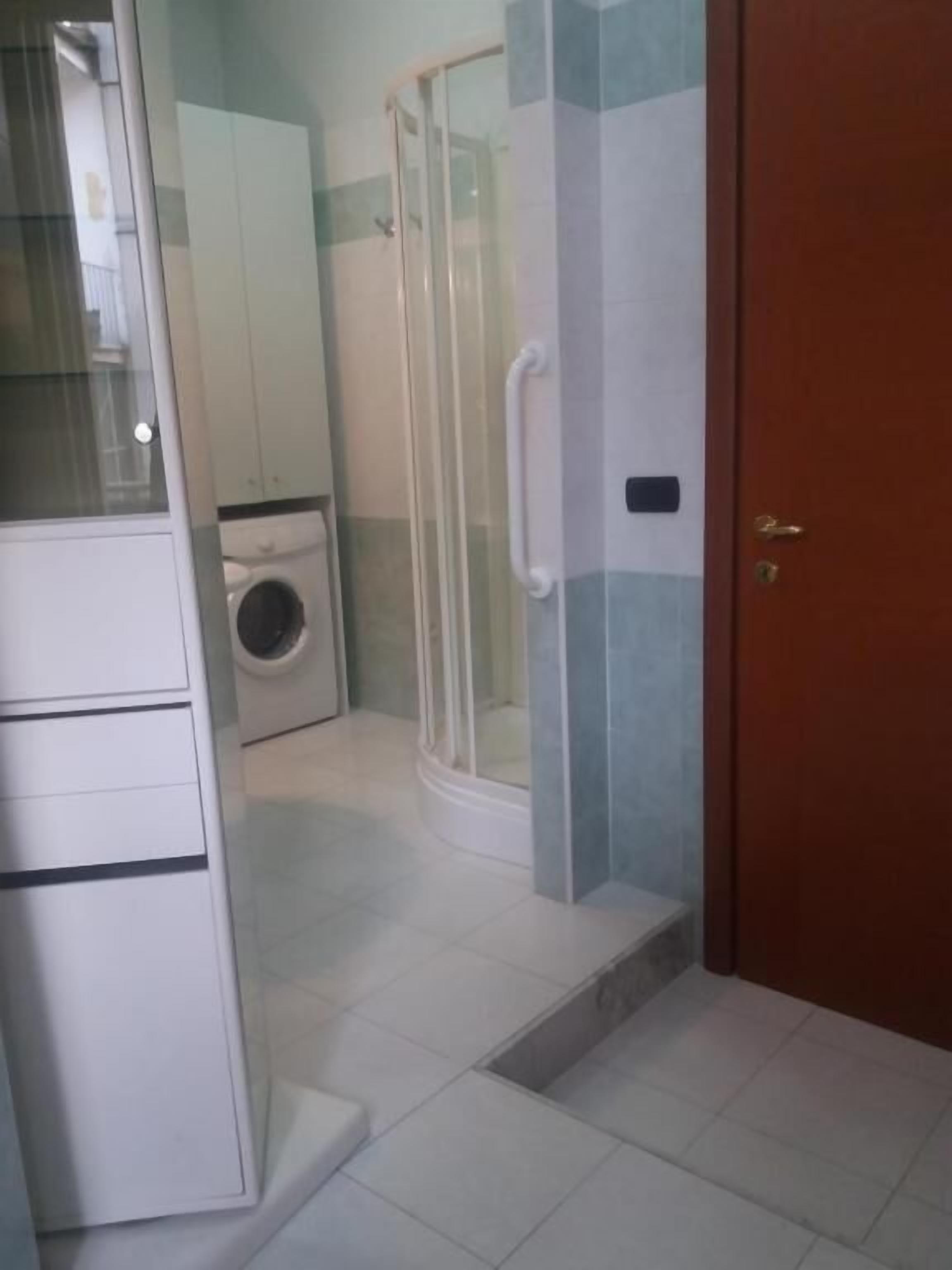 A bathroom with a glass shower enclosure, a washing machine, and a wooden door.