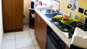 A compact kitchen with wooden cabinets, a gas stove, a sink, and a window providing natural light. - B & B 30 mt dal duomo (Benevento)