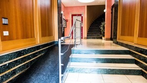 A hotel lobby with a marble staircase, wooden paneling, and a red door at the end. - B & B 30 mt dal duomo (Benevento)