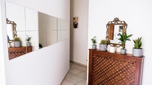 A hallway with a mirrored wall, a wooden cabinet with plants, and a tiled floor. - B & B 30 mt dal duomo (Benevento)