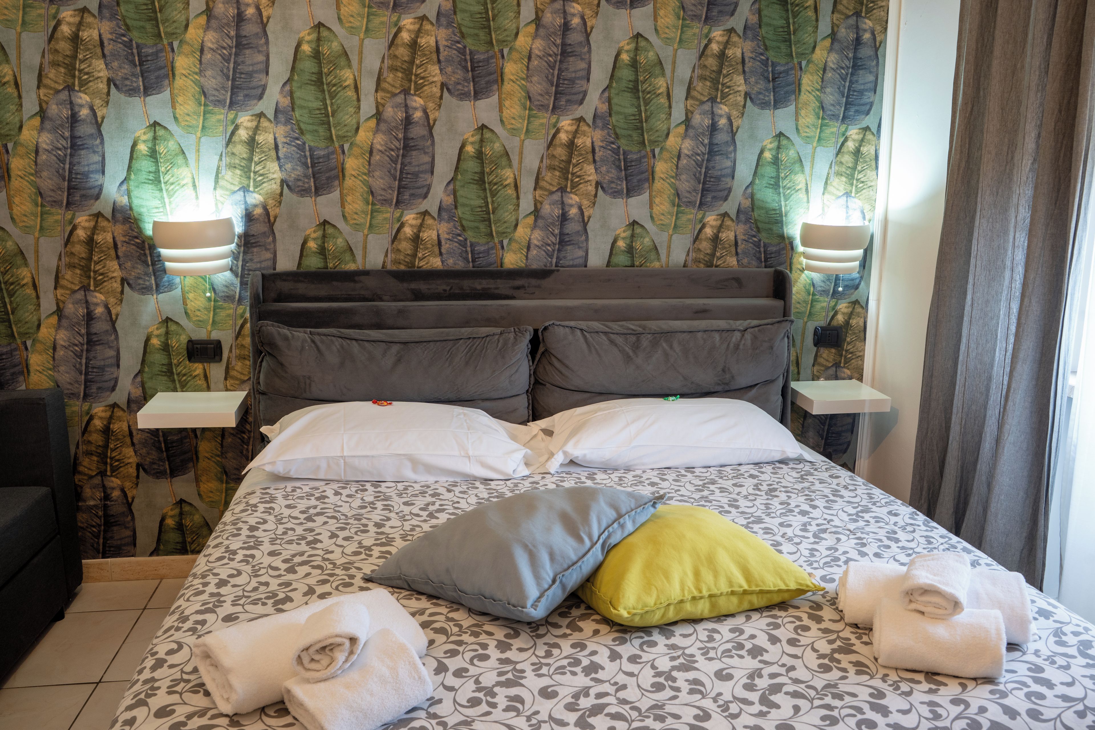 A hotel room with a bed, pillows, a nightstand, a lamp, and a window with curtains.