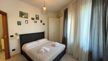 Une chambre d’hôtel avec un lit, un luminaire fixé au mur, une porte et une fenêtre avec des rideaux.