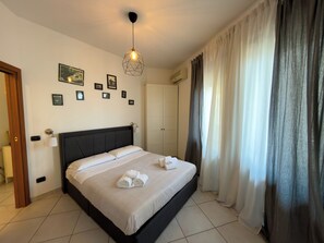A hotel room with a bed, a wall-mounted light fixture, a door, and a window with curtains. - B & B 30 mt dal duomo (Benevento)