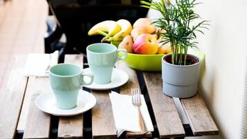 Una mesa de madera con un cuenco verde lleno de fruta, una planta en maceta y una taza y platillo azul claro.