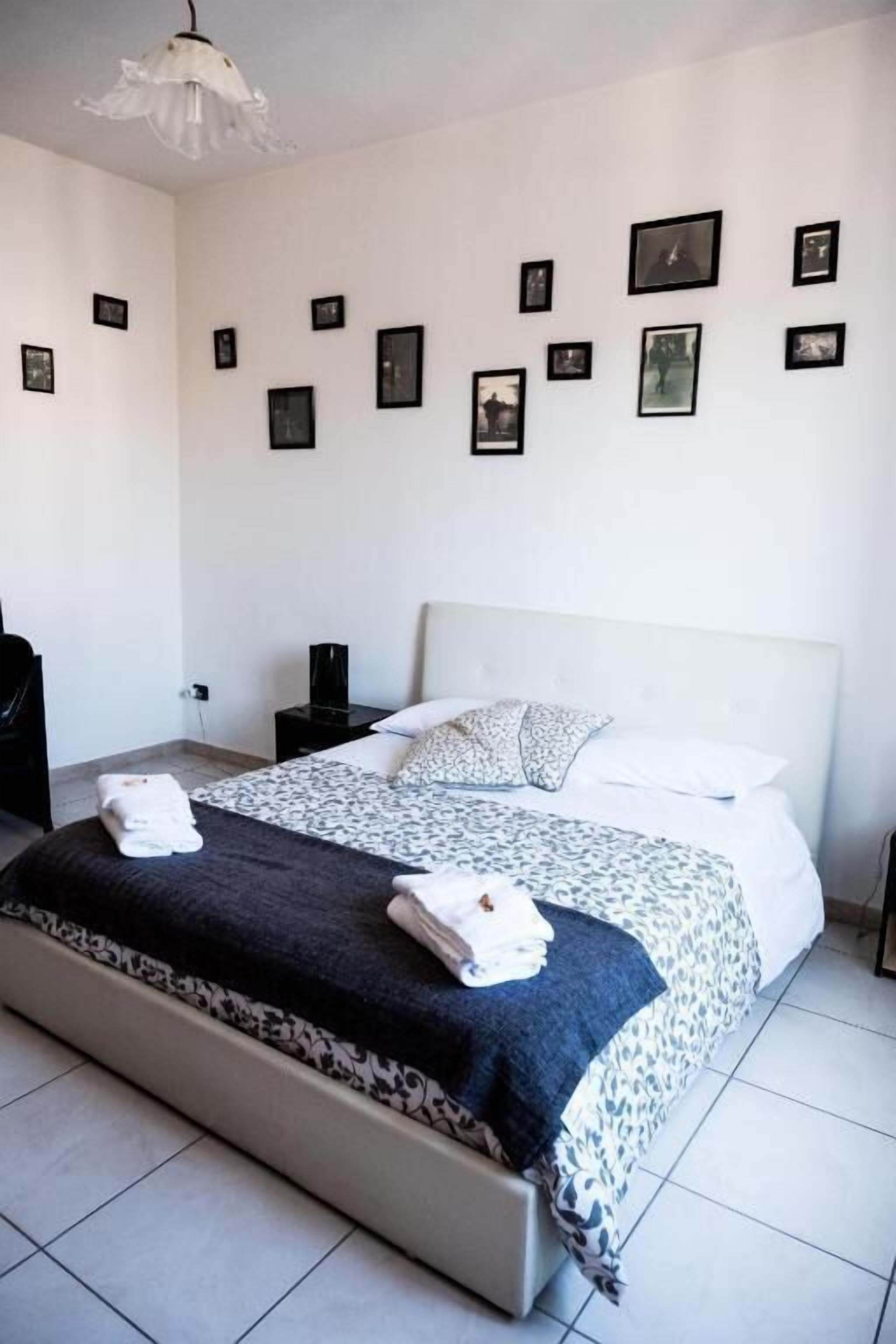 Een netjes ingerichte slaapkamer met een groot bed, een nachtkastje, een stoel, en een muur versierd met ingelijste foto's.