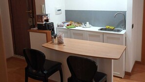 A compact kitchenette with a built-in stove, sink, and white cabinets. There are two black chairs and a small table. - B & B 30 mt dal duomo (Benevento)