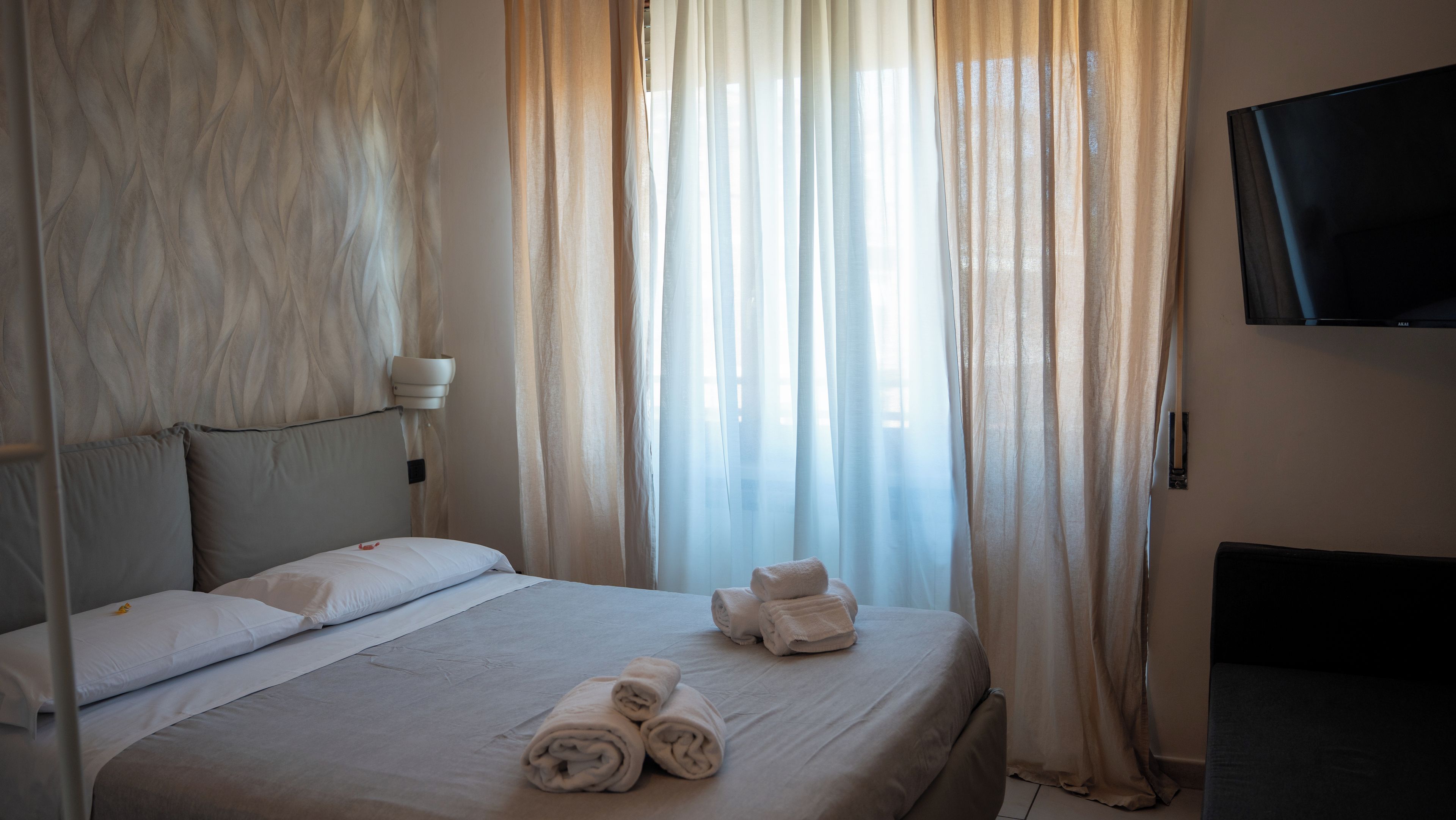 Habitación de hotel con cama, almohadas, televisor y ventana con cortinas.