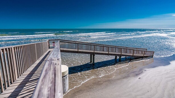 A wooden boardwalk leading to a beach with waves crashing onto the shore. - Easy Beach Access! Charming Beachside Condo! (Galveston)