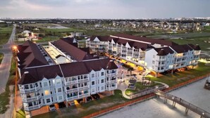 A multi-story hotel with a central courtyard, outdoor seating, and a beach access walkway. - Easy Beach Access! Charming Beachside Condo! (Galveston)