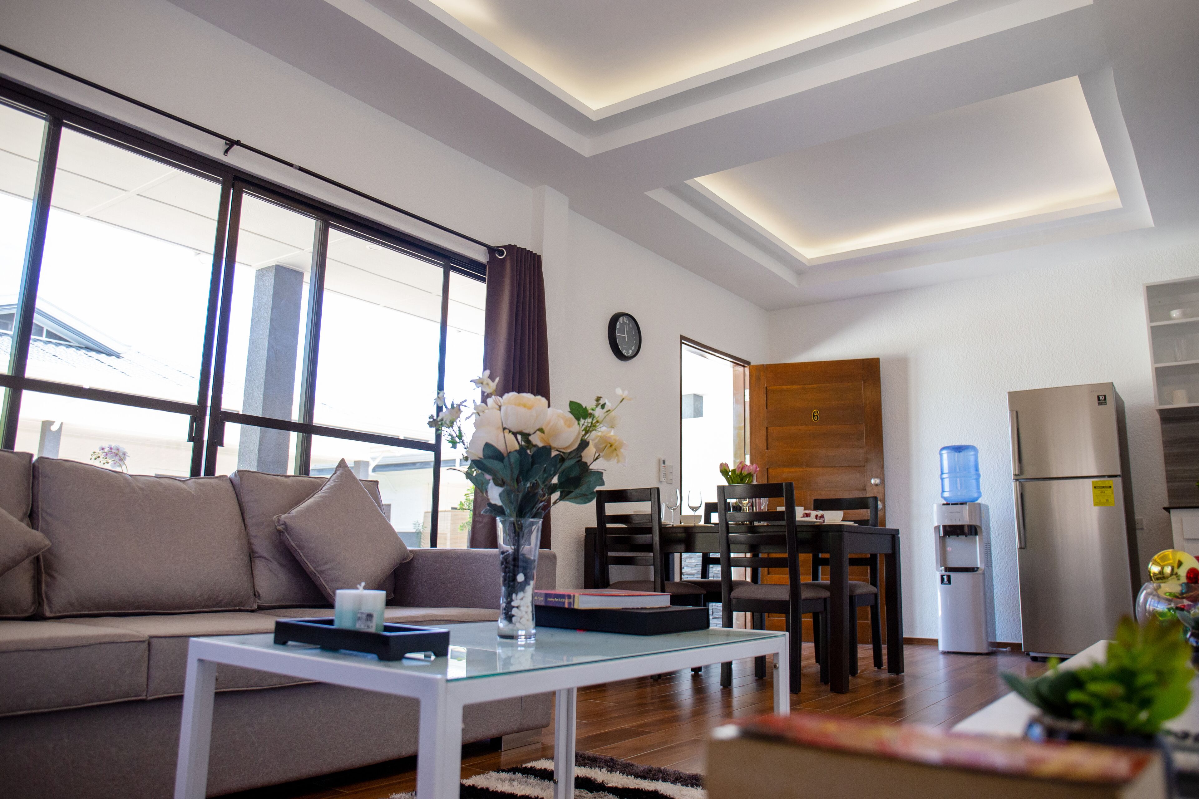 A modern living room with a sofa, a glass coffee table, and a dining area with chairs and a table.