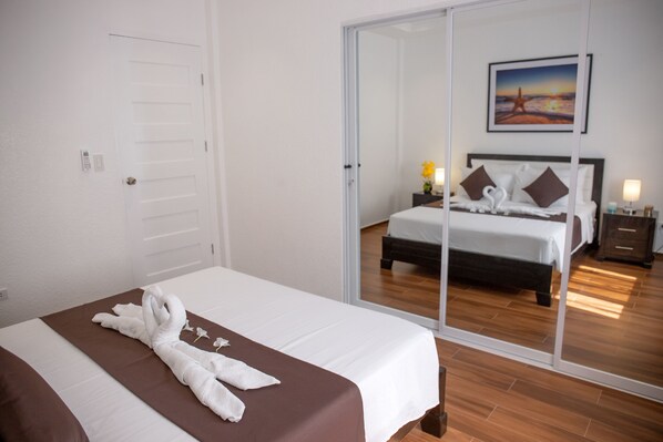 A hotel room with a bed, a sliding glass door leading to another room, a painting on the wall, and a bedside table with a lamp. - Aila Homestay (Panglao)