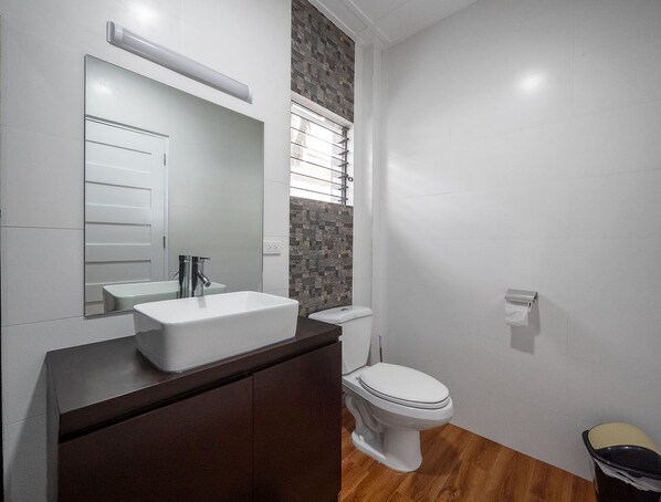 A bathroom with a white sink, a toilet, and a mirror above the sink. - Aila Homestay (Panglao)