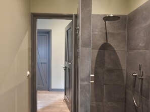 A modern bathroom with a shower, tiled walls, and a wooden door.