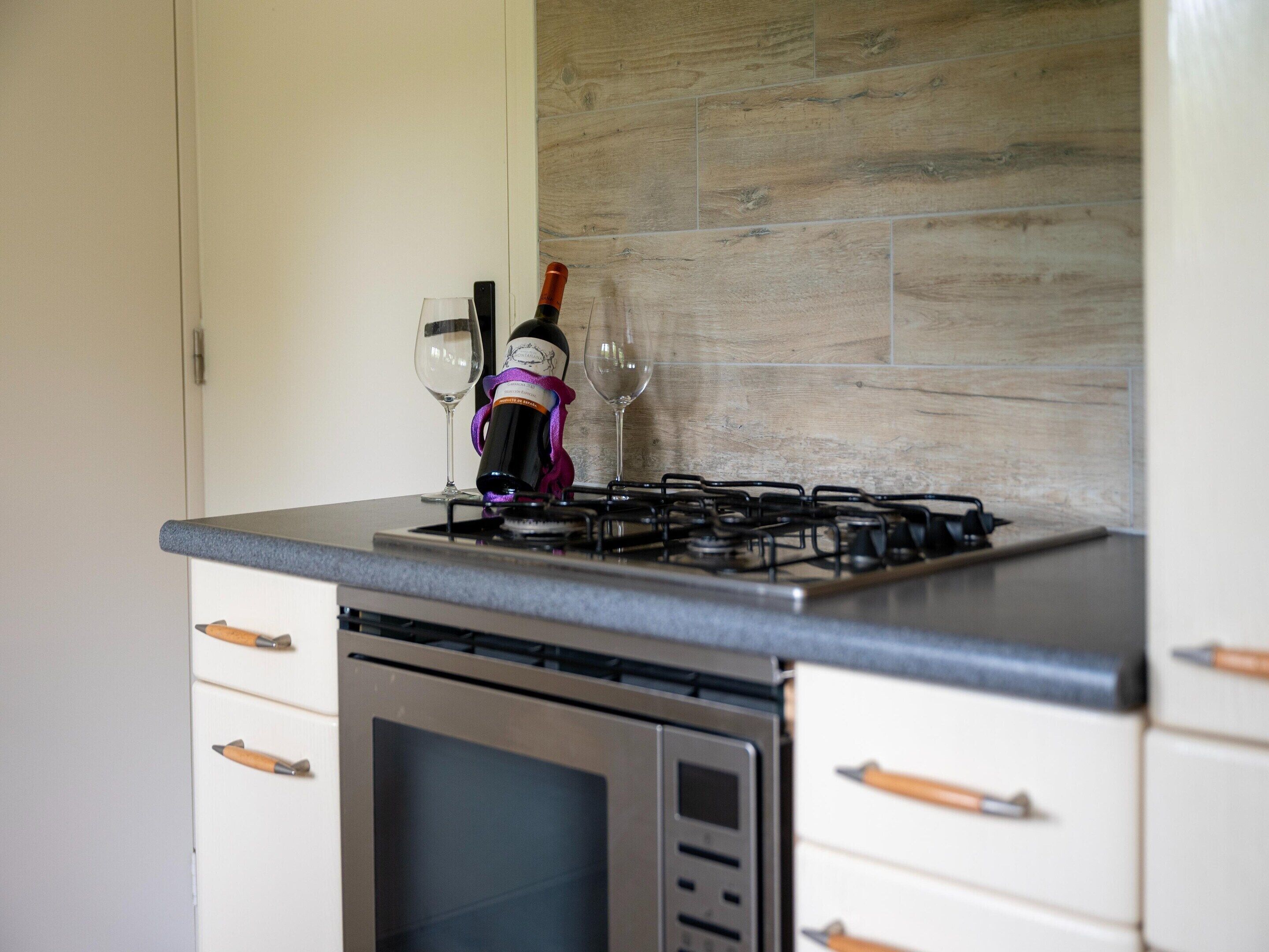 Una cocina con estufa a gas, dos copas de vino y una botella.