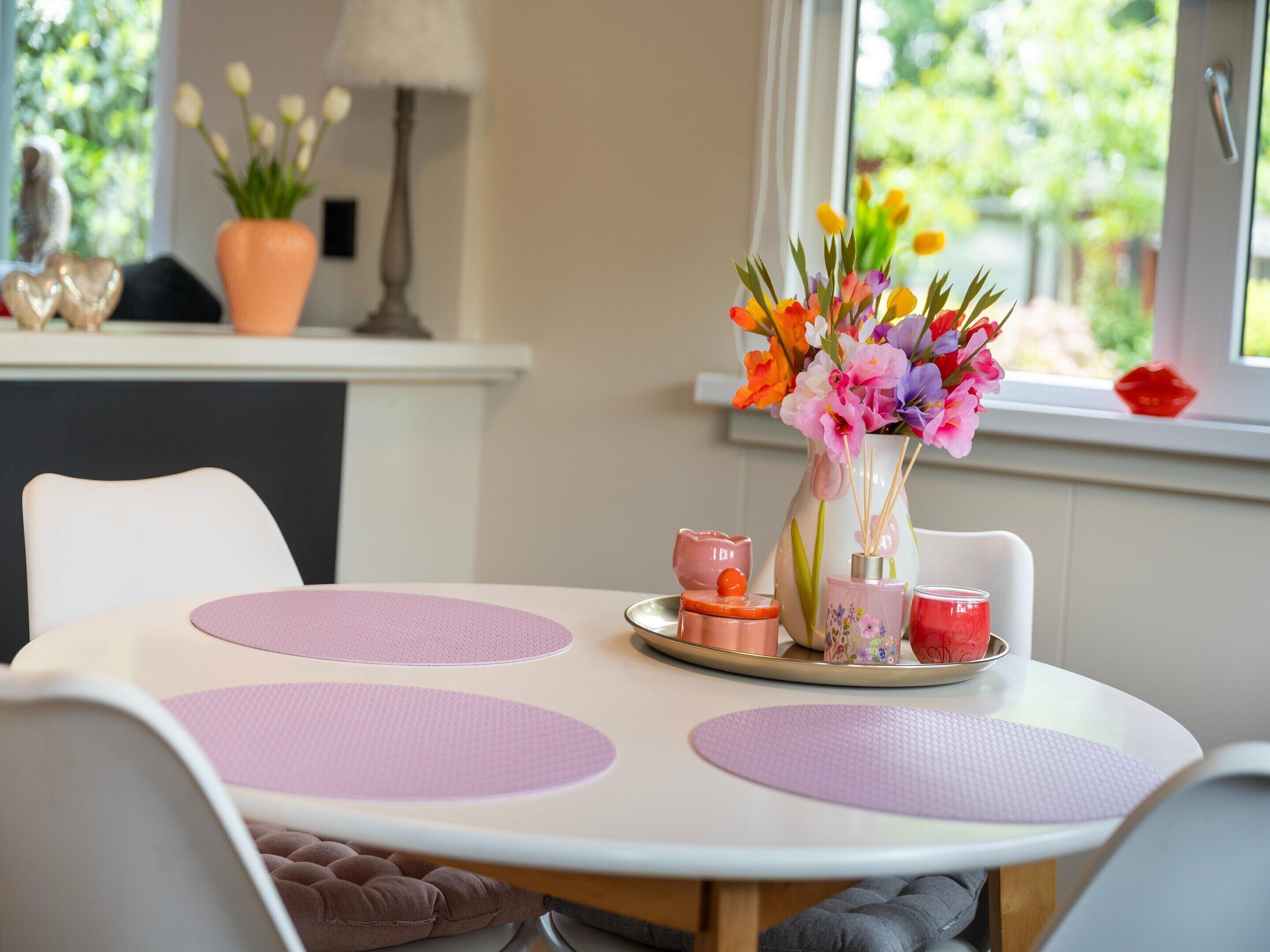 A dining table with a vase of flowers, a lamp, and a window with a view of greenery.