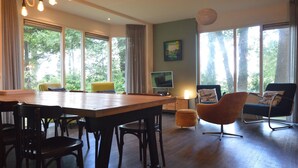 Ett rymligt vardagsrum med ett matbord i trä, flera stolar, en tv och en soffa.