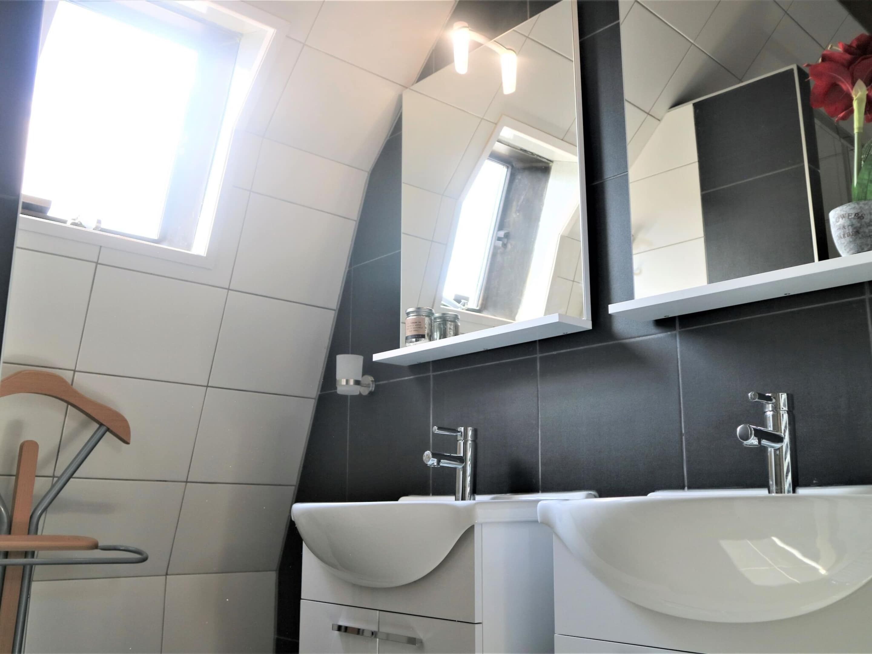 A modern bathroom with two sinks, a mirror, and a window.