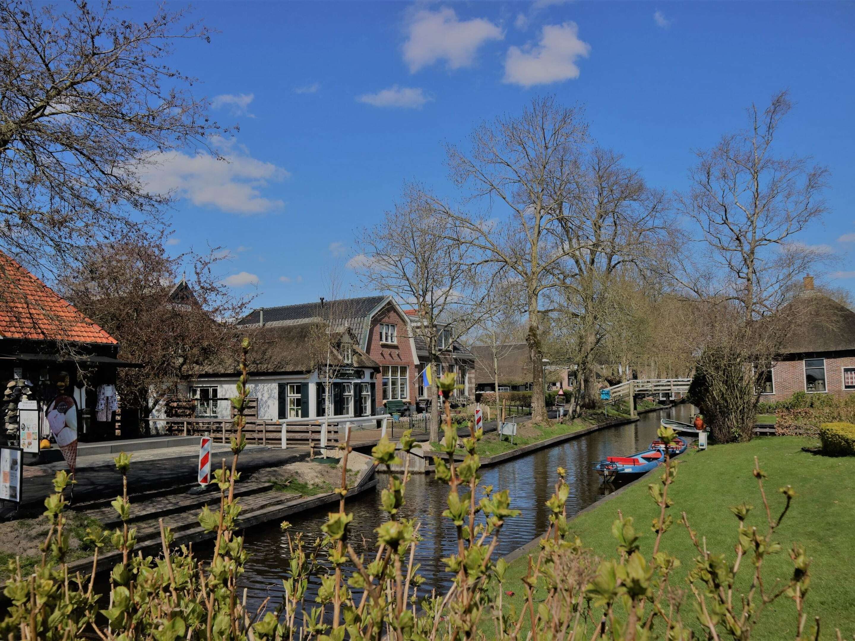 A canal-side building with a traditional thatched roof, a small bridge, and a row of boats along the water.