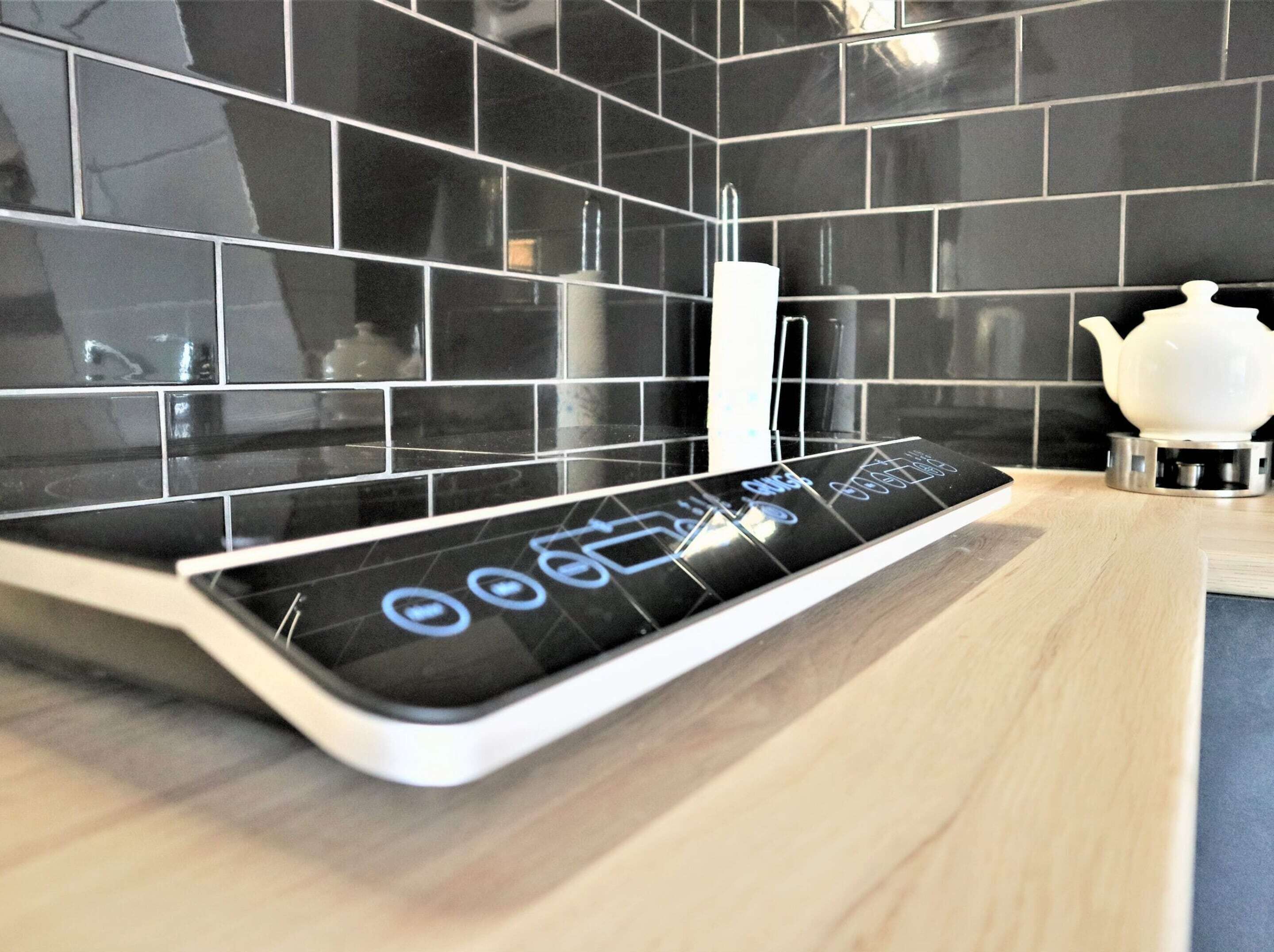 A modern kitchen with black tiled backsplash, a digital control panel, and a white teapot on the counter.