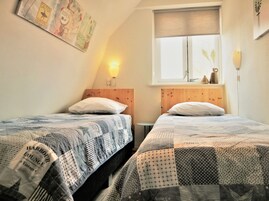 Una habitación con dos camas, cada una con una colcha estampada, un cabecero de madera, una mesita y una ventana con vistas.
