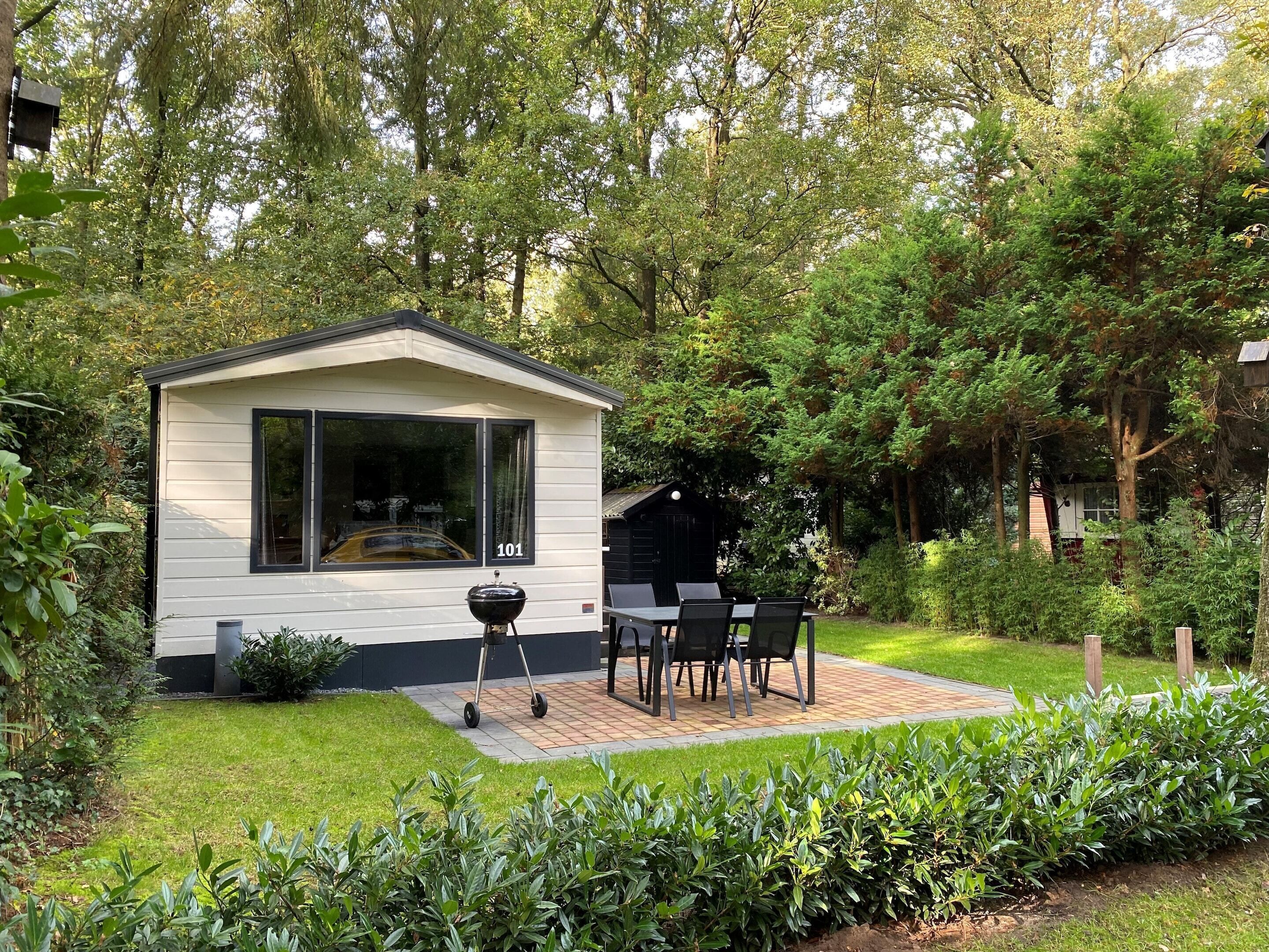 A small, single-story cabin with a large window and a patio area with a grill and outdoor seating.