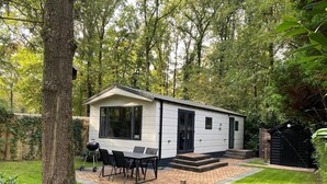 En hyggelig, etetages hytte med terrasse, et bord med stole og grill.