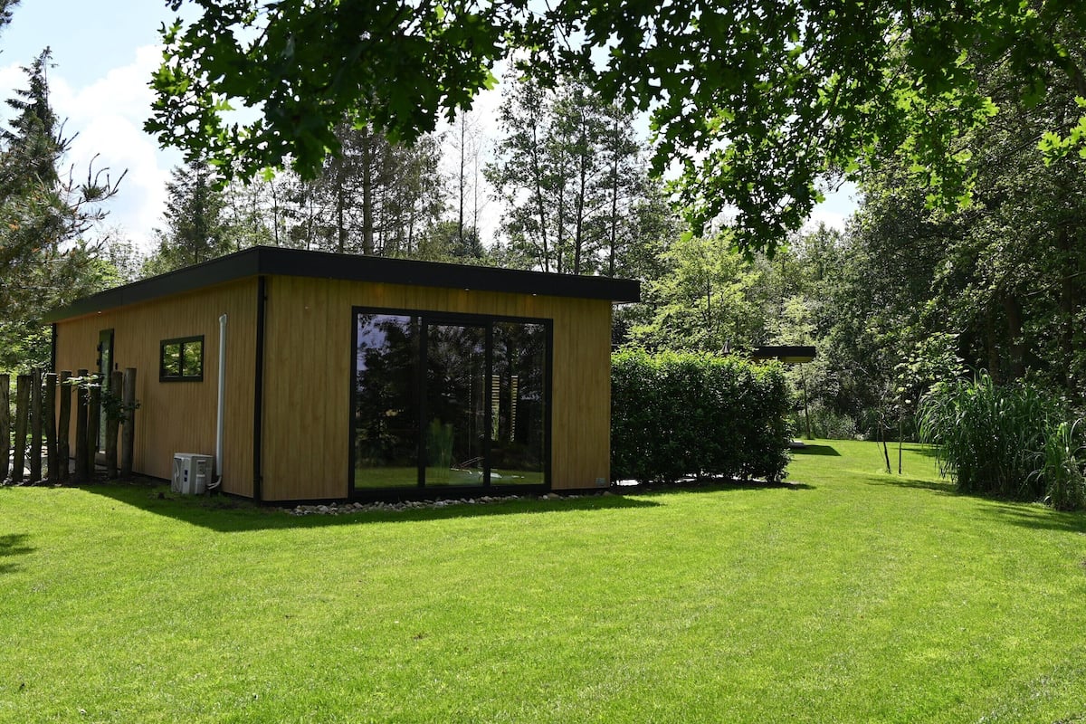 A modern, single-story building with large glass windows, surrounded by a well-maintained lawn and dense trees.
