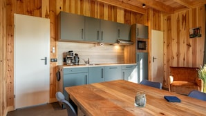 A wooden-paneled kitchen with grey cabinets, a wooden dining table, and a blue chair. - Pleasant Nature Lodge in Dalerveen (Dalerveen)