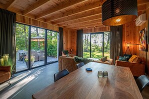 Un intérieur moderne avec une grande table à manger, un plafond en bois et de grandes fenêtres offrant une vue sur l’extérieur.