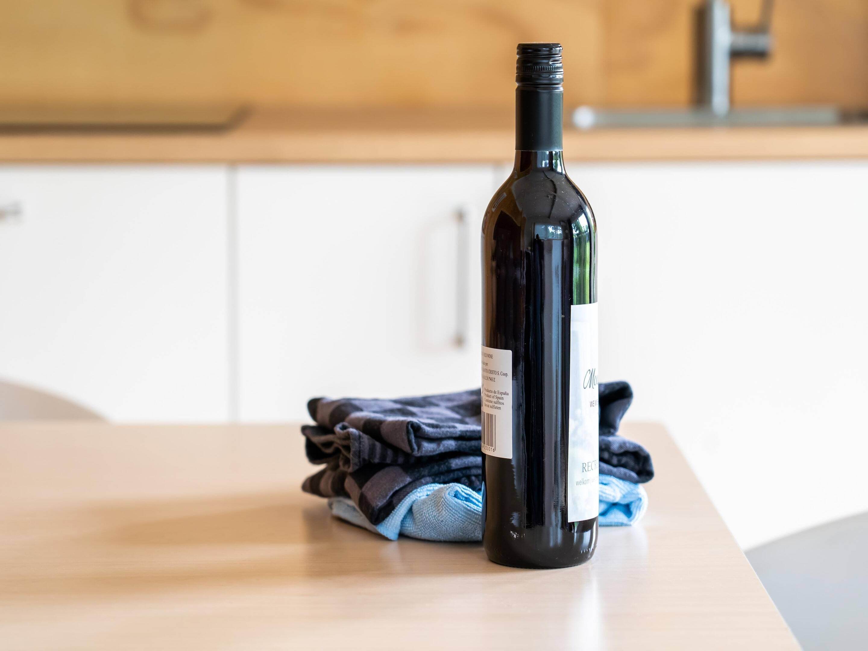 A wine bottle on a wooden table with a folded towel in the background.
