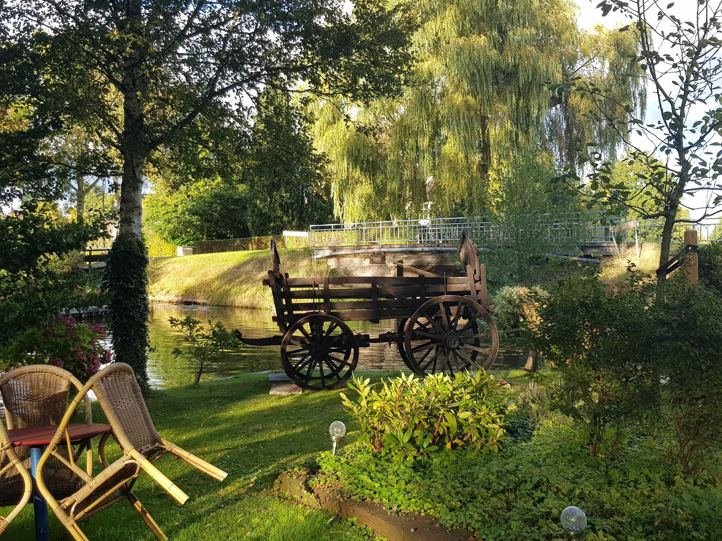 A wooden cart on a bridge over a pond, surrounded by lush greenery and trees.