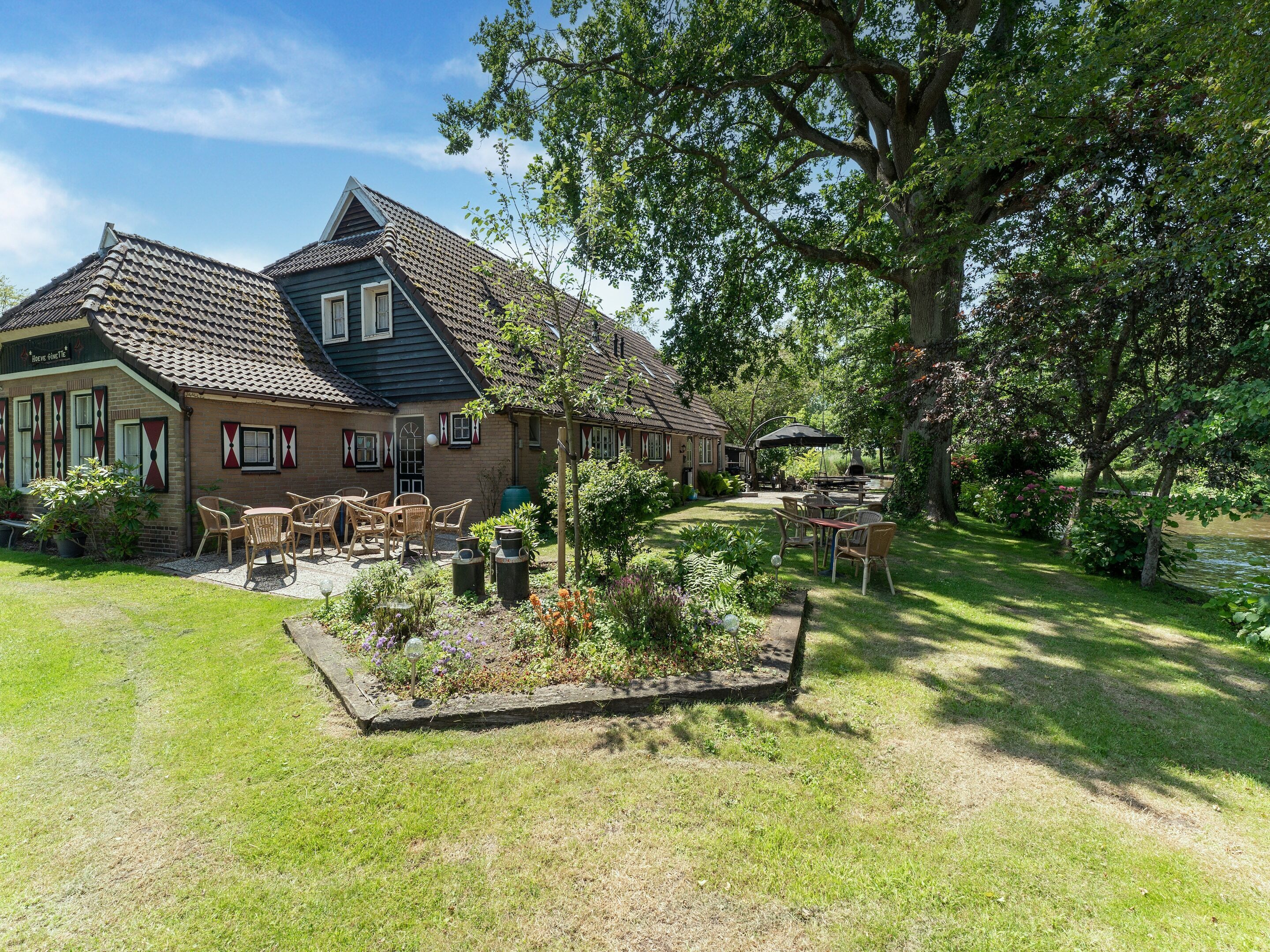 A traditional house with a tiled roof, a garden with outdoor furniture, and a pond.
