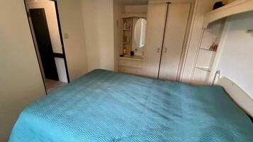A bedroom with a bed, a wardrobe, a mirror, and a shelf with toiletries.