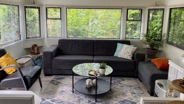 A living room with a dark grey sofa, a glass coffee table, and a patterned rug. - Lovely Chalet in De Pol With Garden (De Pol)
