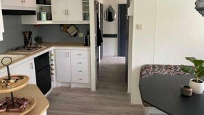 A modern kitchen with white cabinets, a wooden countertop, and a dining area with a black table and a potted plant. - Lovely Chalet in De Pol With Garden (De Pol)