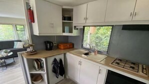 A compact kitchen with white cabinets, a sink, a stove, and a window with blinds. - Lovely Chalet in De Pol With Garden (De Pol)