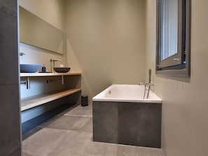 A modern bathroom with a freestanding bathtub, a large mirror, and a built-in sink with a bowl basin.