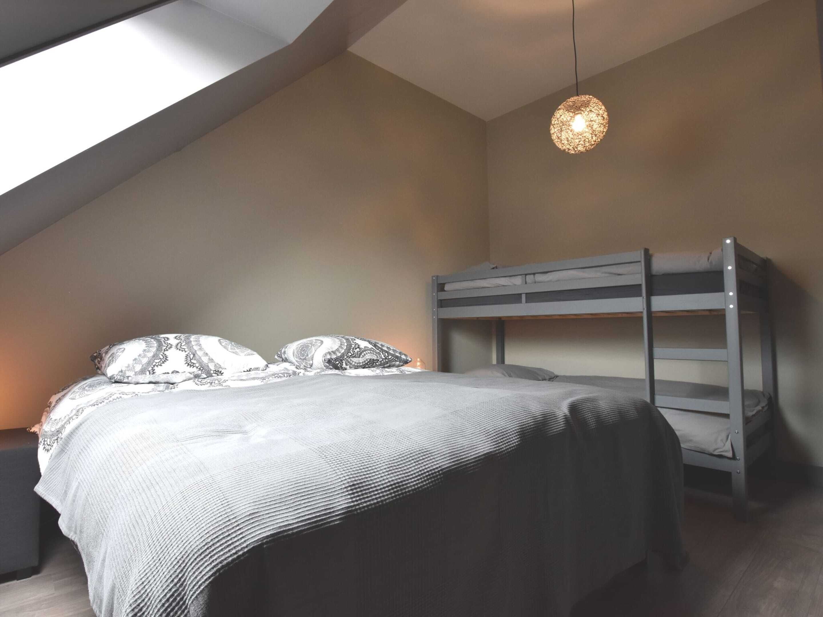A bunk bed in a room with a sloped ceiling, a hanging light fixture, and a window providing natural light.