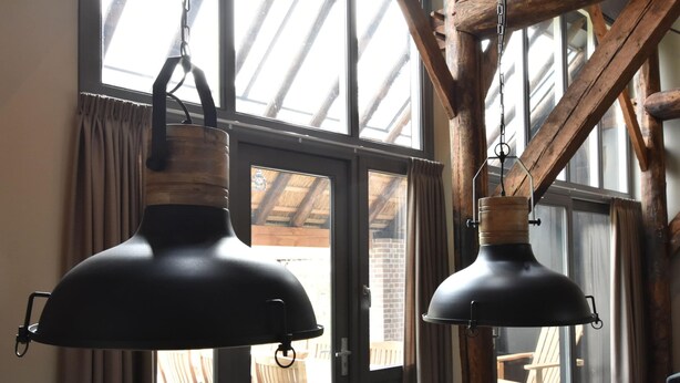 Un área de comedor con una mesa y sillas de madera, ventanas amplias con cortinas, y lámparas colgantes de estilo industrial.