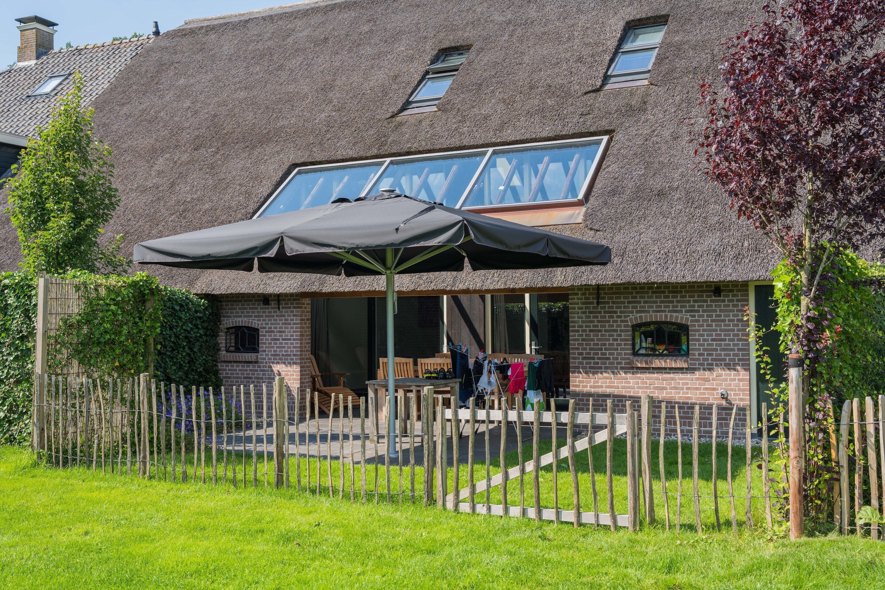 A house with a thatched roof, a covered outdoor seating area, and a wooden fence.