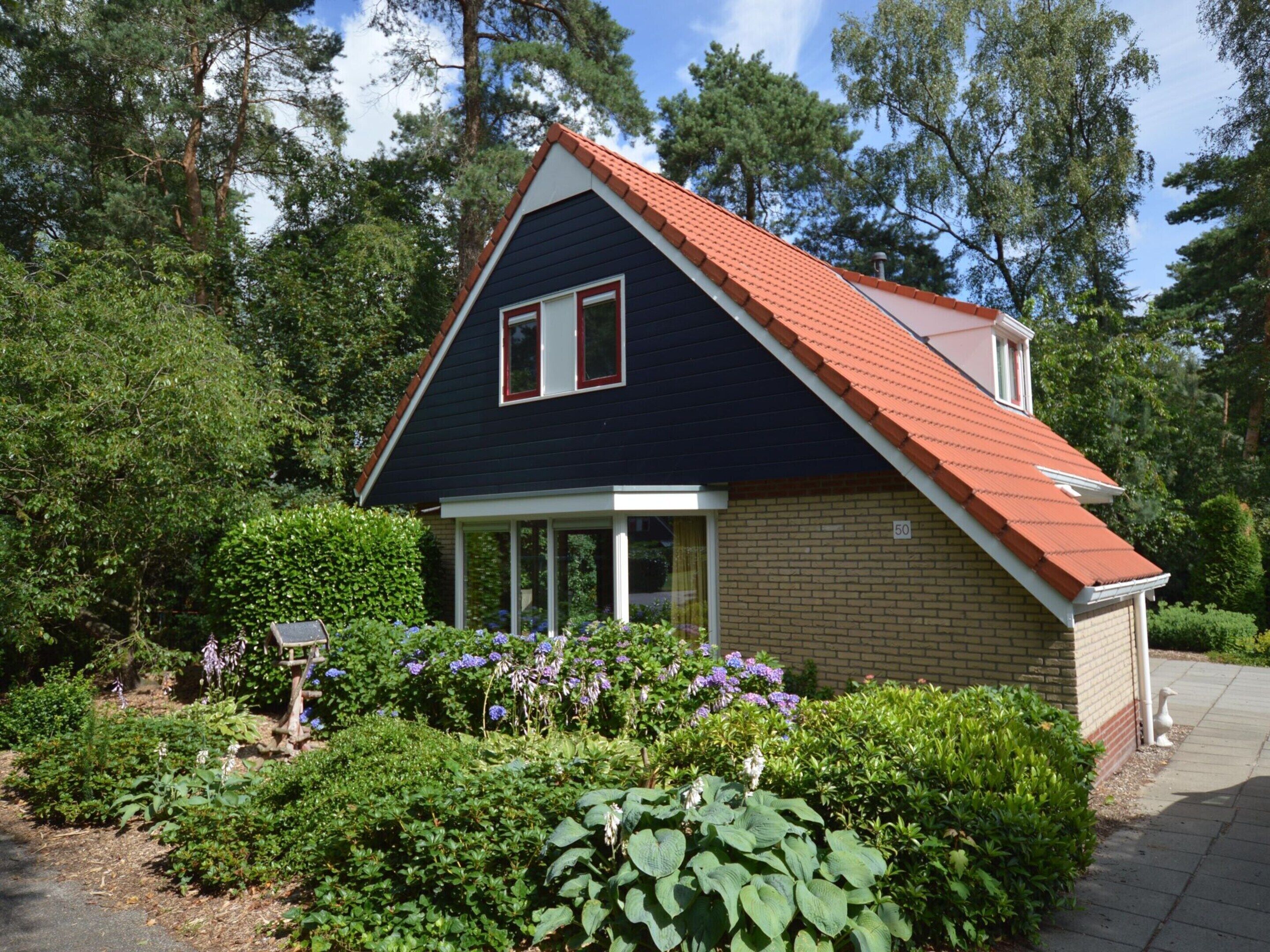 Una casa con fachada azul oscuro, techo rojo y sección de ladrillo. Tiene un pequeño porche con barandilla blanca y una ventana con marco rojo.