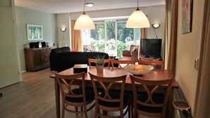 A dining area with a table, chairs, a bowl of fruit, and a television in the background. - Holiday Home Buitenplaats Berg With 5 Rooms (Lemele)