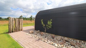 A pathway leading to a building with a corrugated metal exterior, a small tree, and a wooden fence. - Couple Retreat at Unique Nature Lodge (Dalerveen)