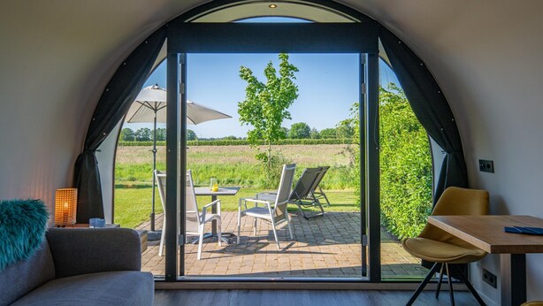 A modern interior with a large arched window, a sofa, a table, and chairs. - Couple Retreat at Unique Nature Lodge (Dalerveen)
