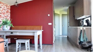 A modern kitchen with wooden cabinets, a dining area with a bench, and a red accent wall. - Peaceful Chalet Close to Norg (Haulerwijk)